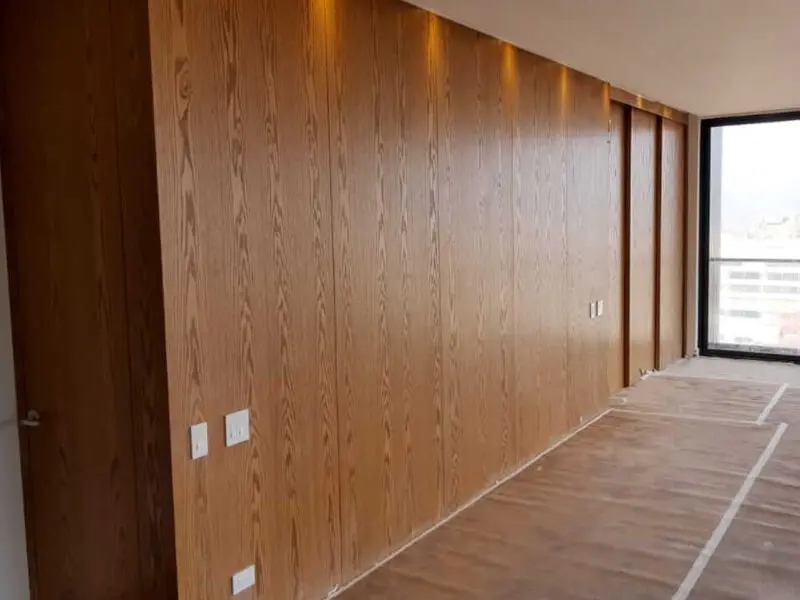 Muro de departamento terminado con paneles de enchapado de madera con veta vertical, un proyecto de terminaciones finas de Ferrenova.