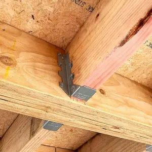 Detalle de un conector metálico estructural (joist hanger) asegurando dos vigas de madera, un accesorio clave para las Medidas de Vigas de Madera para Techos de Ferrenova.