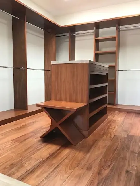 Interior de walk-in closet con módulos, estantes y una isla central, un proyecto modular facilitado por el servicio de corte y enchapado de tableros de Ferrenova.