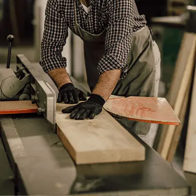 Carpintero de Ferrenova realizando un canteado de madera, pasando un tablón por una máquina canteadora (jointer) en el taller.