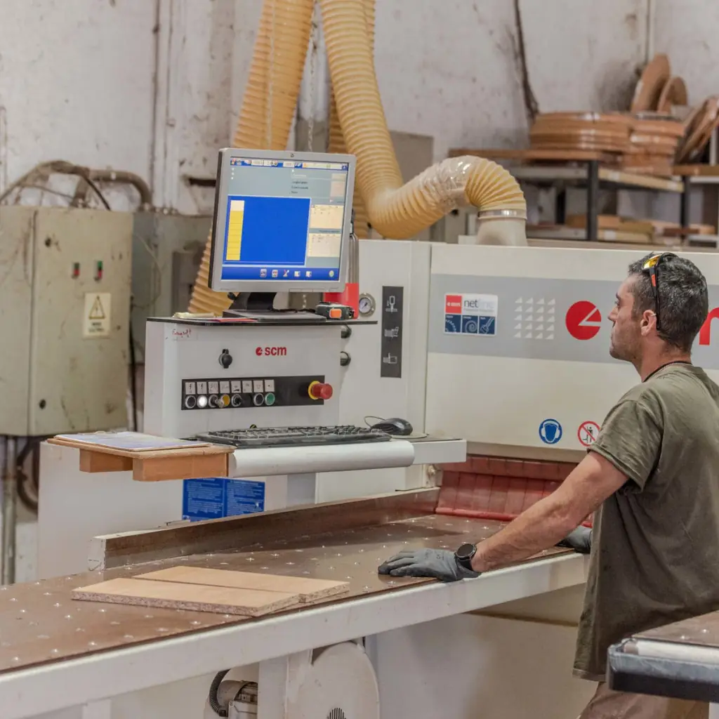 Máquina canteadora industrial de color azul realizando el Canteado de Madera de un tablón aserrado,