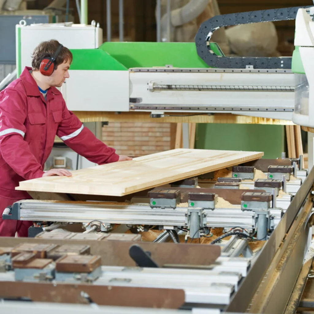 Obrero de carpintería utilizando una máquina CNC para procesar una plancha de Madera Dimensionada, asegurando la pieza para un corte o fresado de precisión.