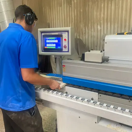 Operario de Ferrenova aplicando tapacantos en una pieza de melamina, servicio complementario al corte de madera.